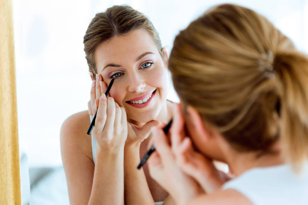 Красивая молодая женщина делает макияж возле зеркала дома
. - Фото, изображение
