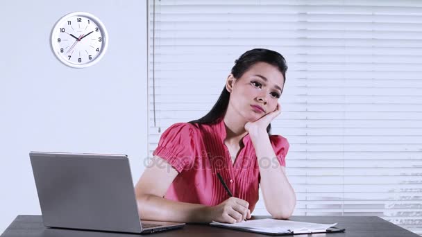 Businesswoman working in the office and looks bored, writing on a paperwork with laptop on desk - Imágenes, Vídeo