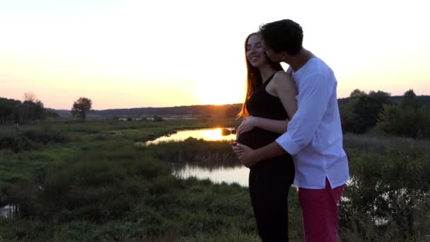 L'uomo abbraccia la sua moglie incinta al tramonto al rallentatore
. - Filmati, video