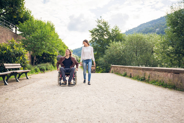 pareja joven en silla de ruedas paseando por el parque - Foto, Imagen
