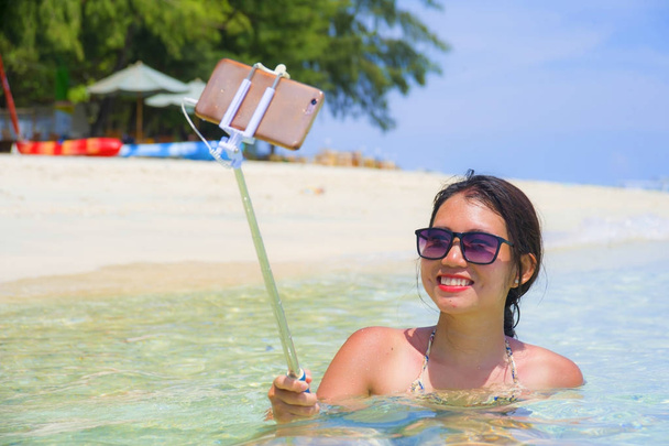 nuori kaunis ja onnellinen aasialainen kiinalainen nainen hauskaa merivedellä ottaen selfie kuva matkapuhelin kamera paratiisi rannalla
 - Valokuva, kuva
