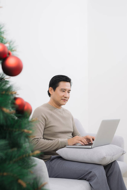 Homme avec ordinateur portable assis sur le canapé à l'arbre de Noël
 - Photo, image