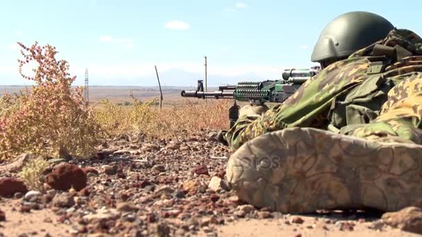 no capacete militar apontando uma metralhadora, deitada na areia em emboscada
 - Filmagem, Vídeo