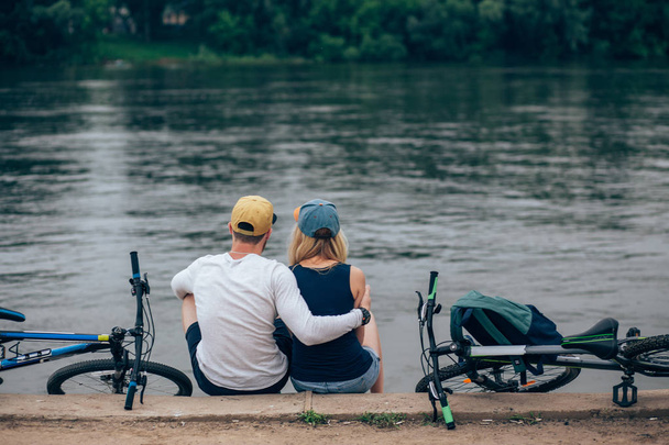 Ρομαντικό ζευγάρι με ποδήλατα χαλαρώνοντας στο ηλιοβασίλεμα στη λίμνη. Εμπίπτουν στην έννοια της αγάπης. - Φωτογραφία, εικόνα