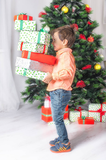 the boy holds in hand many gifts at a  Cristmas fir tree - Foto, Imagem