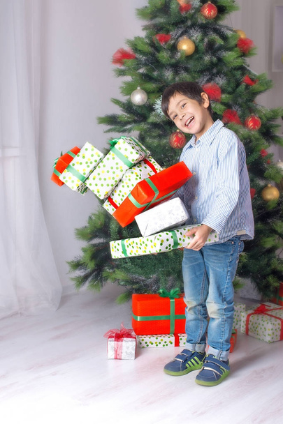 the boy holds in hand many gifts at a  Cristmas fir tree - Foto, immagini