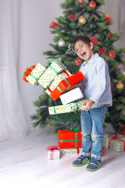 the boy holds in hand many gifts at a  Cristmas fir tree - Foto, Imagen