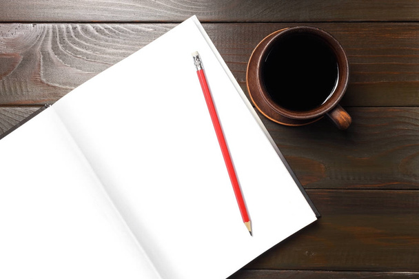 Forró fekete kávé barna csészében és jegyzetfüzet fehér tiszta lapokkal, hely a szövegnek, piros ceruza sötét fa munkaasztalon, felülnézet. - Fotó, kép