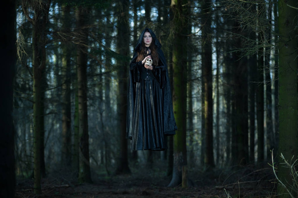 Witch with a skull levitating in the forest - Фото, изображение