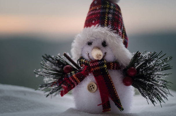 New Year Christmas concept. The snowman stands on snow with blurred nature background. White snowman surrounded by Christmas trees on evening background. Toy Decoration. Selective focus - Photo, Image