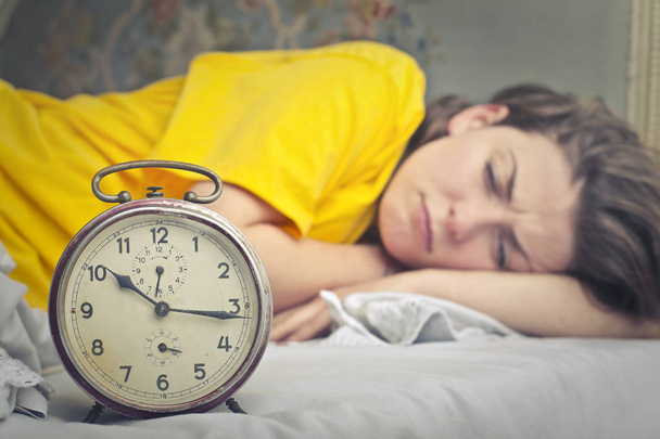 Tired girl in bed looking ahh alarm clock - Foto, Imagen