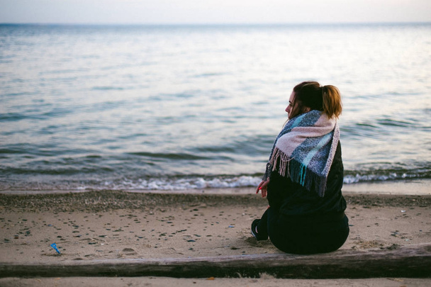 woman on a cold day wrapped in a scarf on the beach, at sunset autumn - Foto, Imagem