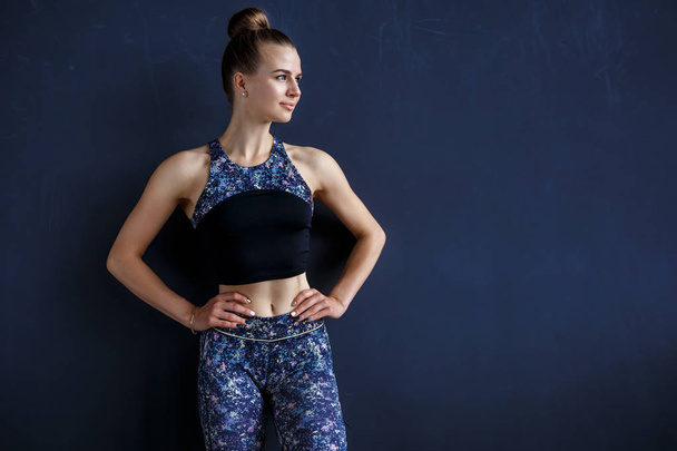 Beautiful fitness model is posing in front of the dark wall in a dark training suit - Foto, Bild