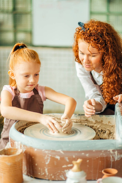 redhead mother and her child daughter moulding with clay on pottery wheel - Zdjęcie, obraz