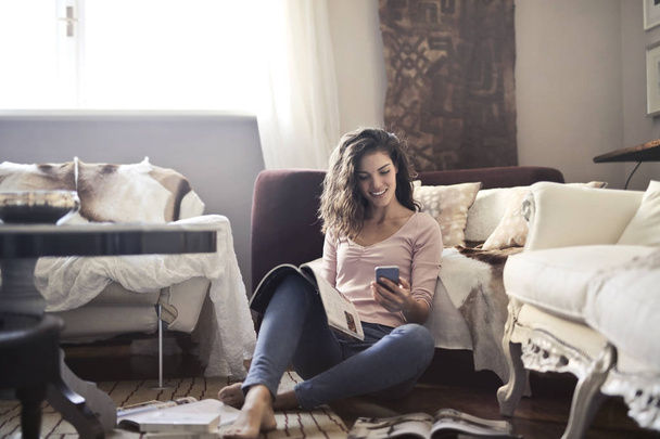 Girl in a living room reading a magazine and using a smartphone - Fotoğraf, Görsel
