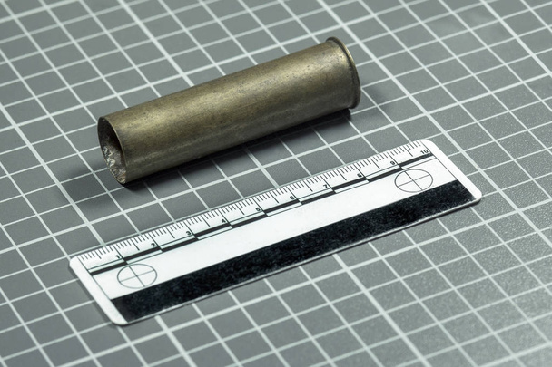 De schot cartridge van het geweer en de forensische liniaal liggen op een groene achtergrond met witte lijnen voor ballistische onderzoek. Close-up. - Foto, afbeelding