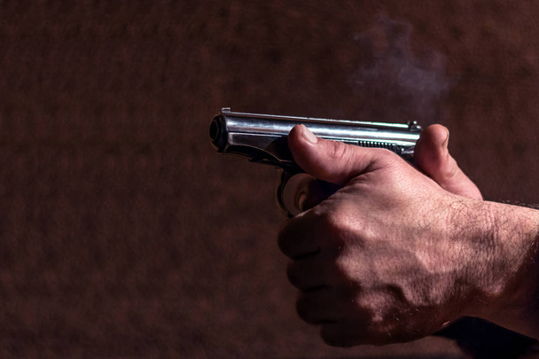 Shot of a gun in the hands of a man on a brown background. Close-up. - Фото, изображение