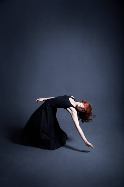 Dancer in a black dress is dancing in the dark studio - Foto, Bild