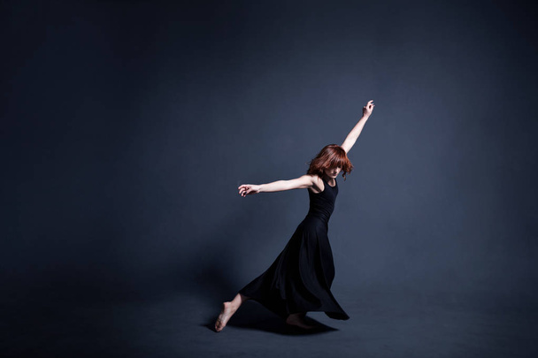 Dancer in a black dress is dancing in the dark studio - Foto, afbeelding