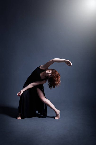 Dancer in a black dress is dancing in the dark studio - Foto, imagen