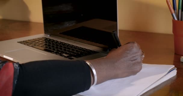 Mature African American woman writing in a notebook next to her laptop - Felvétel, videó