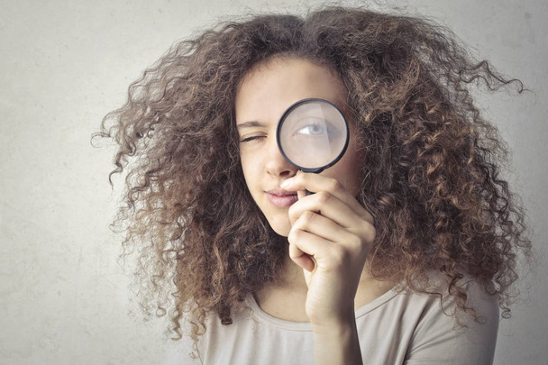 Girl with curly hair looking through a magnifying glass - Фото, зображення
