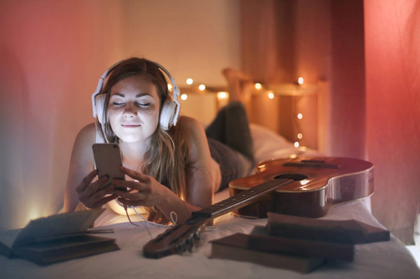 A girl relaxing on her bed listening to music with headphones - Photo, Image