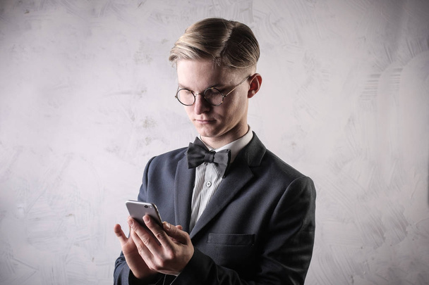 Portrait of a young elegant man with glasses using a smartphone - Фото, изображение