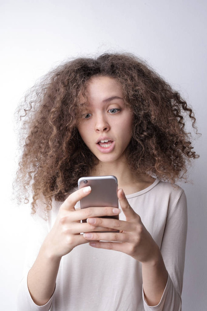 Portrait of a girl with curly hair using her smartphone with a surprised expression - Fotografie, Obrázek