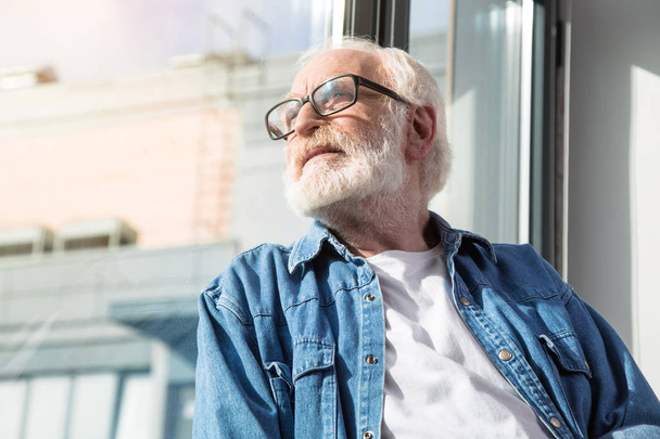 Dreamy old man sitting at home and enjoying sunny weather - Foto, Imagem