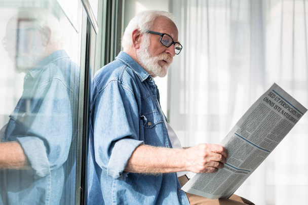Wise aged man holding journal while based on windowsill - 写真・画像