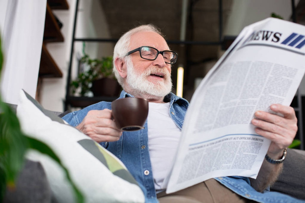 Senior man enjoying fresh news sitting at home with drink - Foto, Imagen