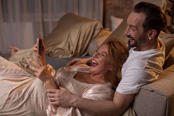 Joyful married couple laughing at video on gadget - Фото, изображение