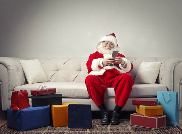 Santa Claus sitting on a sofa and looking at the phone - 写真・画像