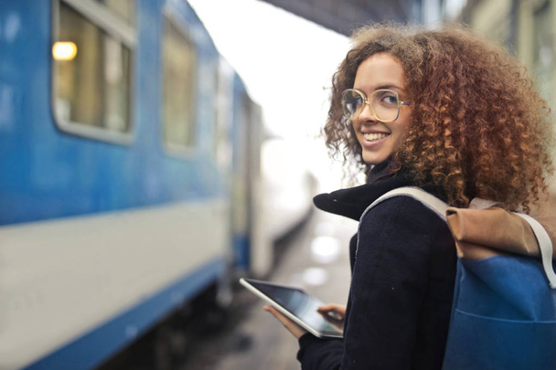 Smiling girl with a tablet in her hand and a backpack waiting at a train station - Foto, immagini