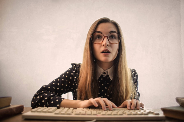 Young woman with glasses texting on a keyboard  - Foto, Bild