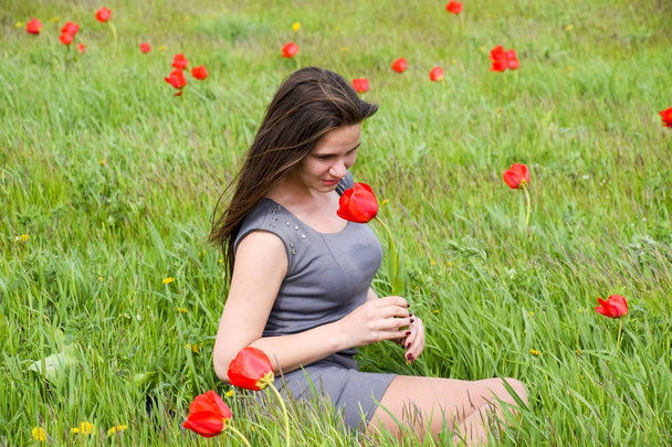Beautiful fairy young girl in a field among the flowers of tulips. Portrait of a girl on a background of red flowers and a green field. Field of tulips. - Foto, immagini