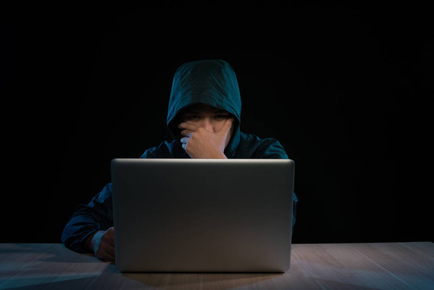 Hacker in a dark hoody sitting in front of a notebook. Computer privacy attack - Фото, изображение