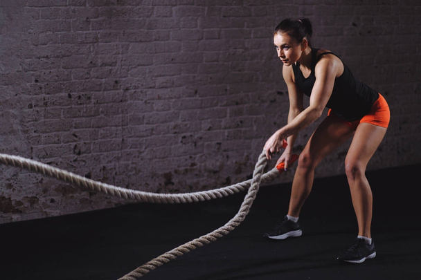 Battle ropes session. Attractive young fit and toned sportswoman training in gym - Фото, изображение