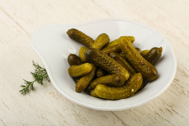 Pickled cucumbers in bowl over wooden background  - Photo, Image