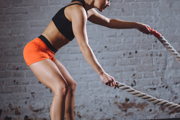 close up photo of woman doing Battle rope workout near white brick wall - Photo, image