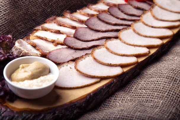 Gesneden stukjes gerookte varkensvlees, kalfsvlees en varkensvlees "briskets" aangeduide met mosterd en paard-radijs op houten bord - Foto, afbeelding
