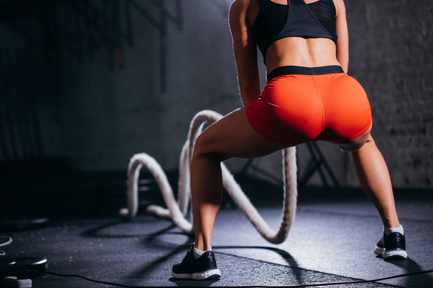 rear view of tonned woman training with battle rope in cross fit gym - Foto, Imagem