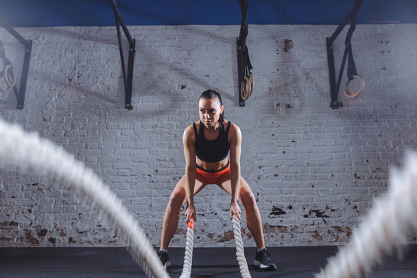 Attractive young fit and toned sportswoman working out with battle ropes - Foto, immagini