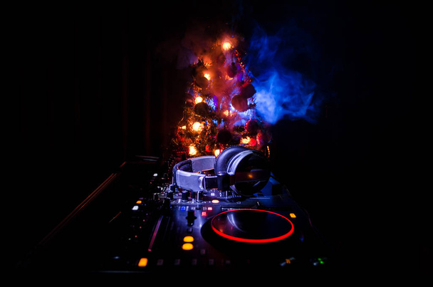 DJ mixer met koptelefoon op donkere nachtclub achtergrond met kerstboom New Year Eve. Close-up van Nieuwjaar elementen of symbolen (Kerstman, sneeuwman, hond 2018, luxe-geschenketui) op een Dj-tafel. - Foto, afbeelding