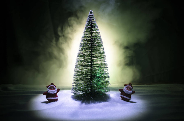 Boneca Feliz Papai Noel na época de Natal com árvore e neve. Fundo bokeh colorido. Papai Noel e Feliz Natal modelo figura brinquedo no fundo enevoado tonificado escuro
 - Foto, Imagem