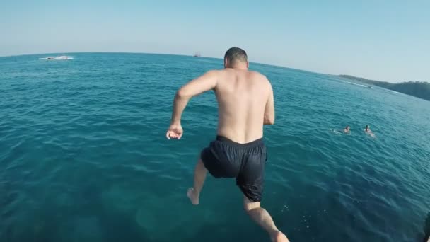 A funny view of a middle-aged man in black shorts jumping feet first in the turquoise waters on a Turkish resort in summer in slo-mo - Felvétel, videó