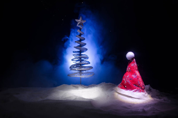 サンタ クロースの帽子と雪の背景にぼやけクリスマス ツリー クリスマス休日新年背景。休日の属性を持つ新しい年概念イメージ装飾。濃い霧のフィルター化 - 写真・画像