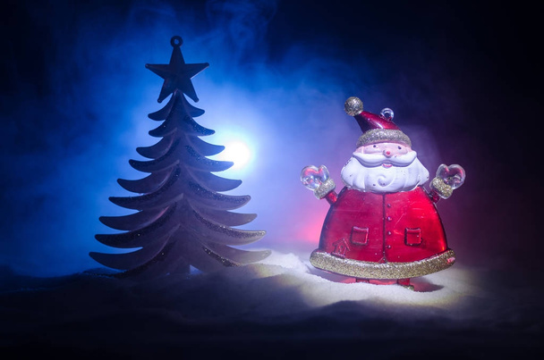Joyeux Père Noël poupée sur le temps de Noël avec arbre et neige. Fond bokeh coloré. Santa Clause et Joyeux Noël modèle figurine jouet sur fond brumeux ton foncé. Concentration sélective
 - Photo, image