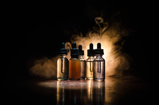Vape concept. Smoke clouds and vape liquid bottles on dark background. Light effects. Useful as background or vape advertisement or vape background. - Photo, image